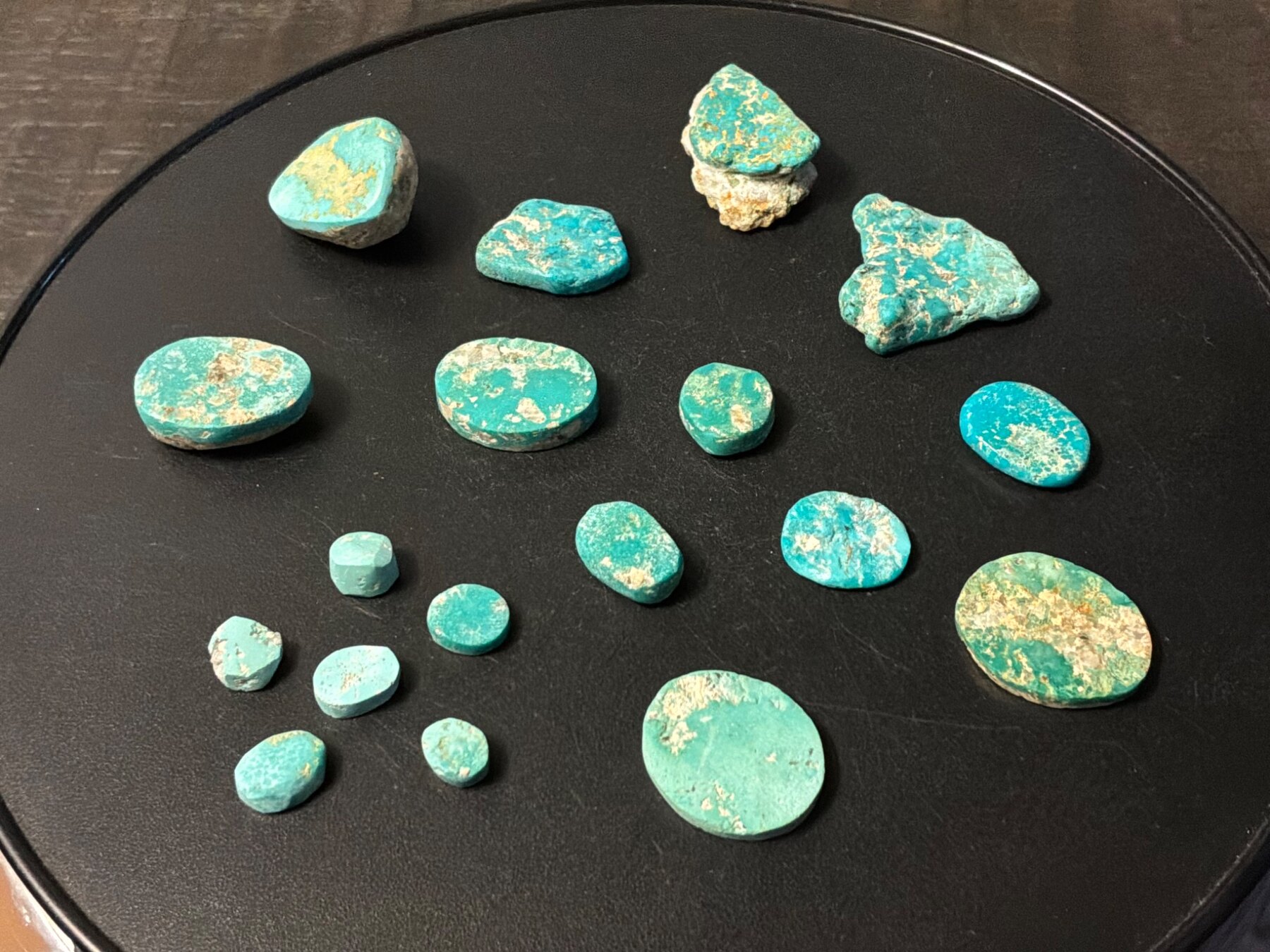 Seventeen hand-polished and natural Leadville turquoise pieces on a black background